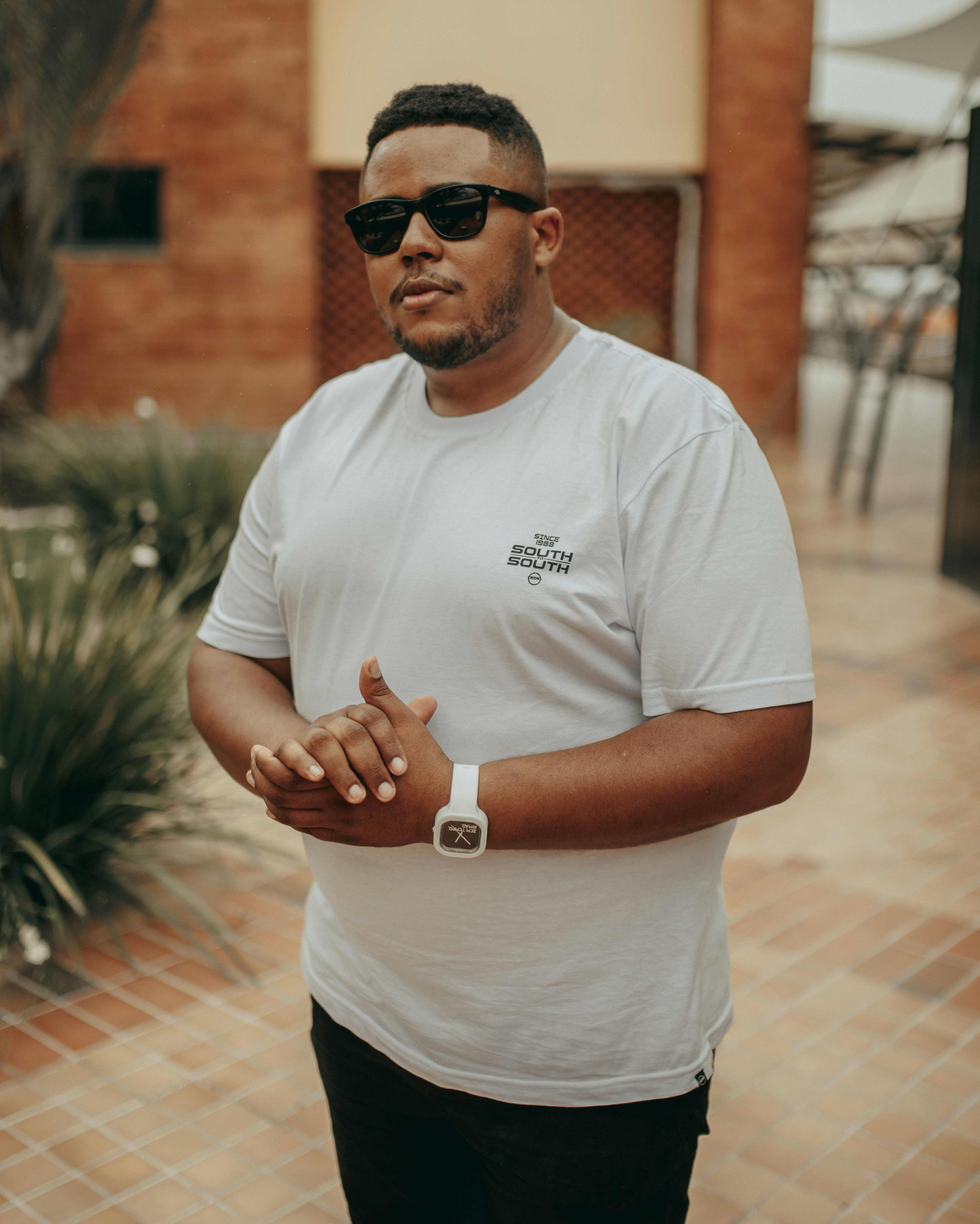 man in white crew neck t-shirt and black sunglasses standing on brown brick floor during