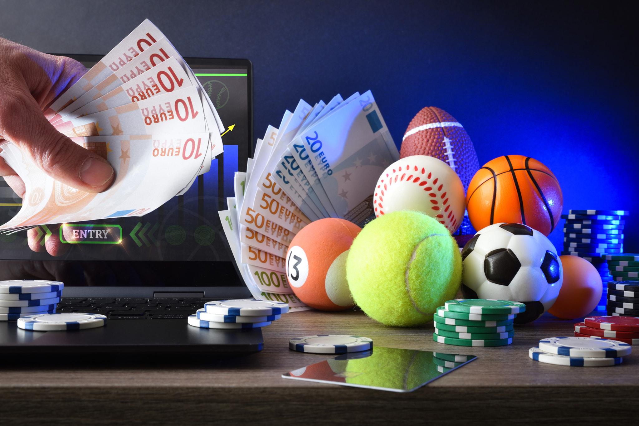 Person making online sports bets on desk with sport objects